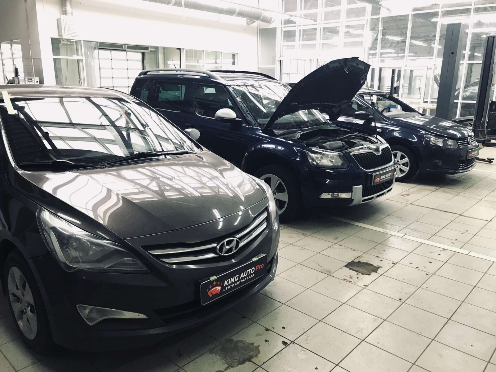 Несколько автомобилей в светлом боксе: Hyundai Solaris, Škoda, Volkswagen