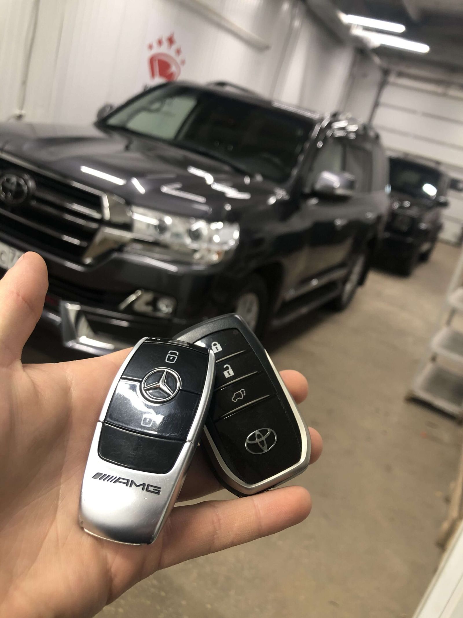 Ключи Mercedes и Toyota в руке мастера на фоне Land Cruiser 200