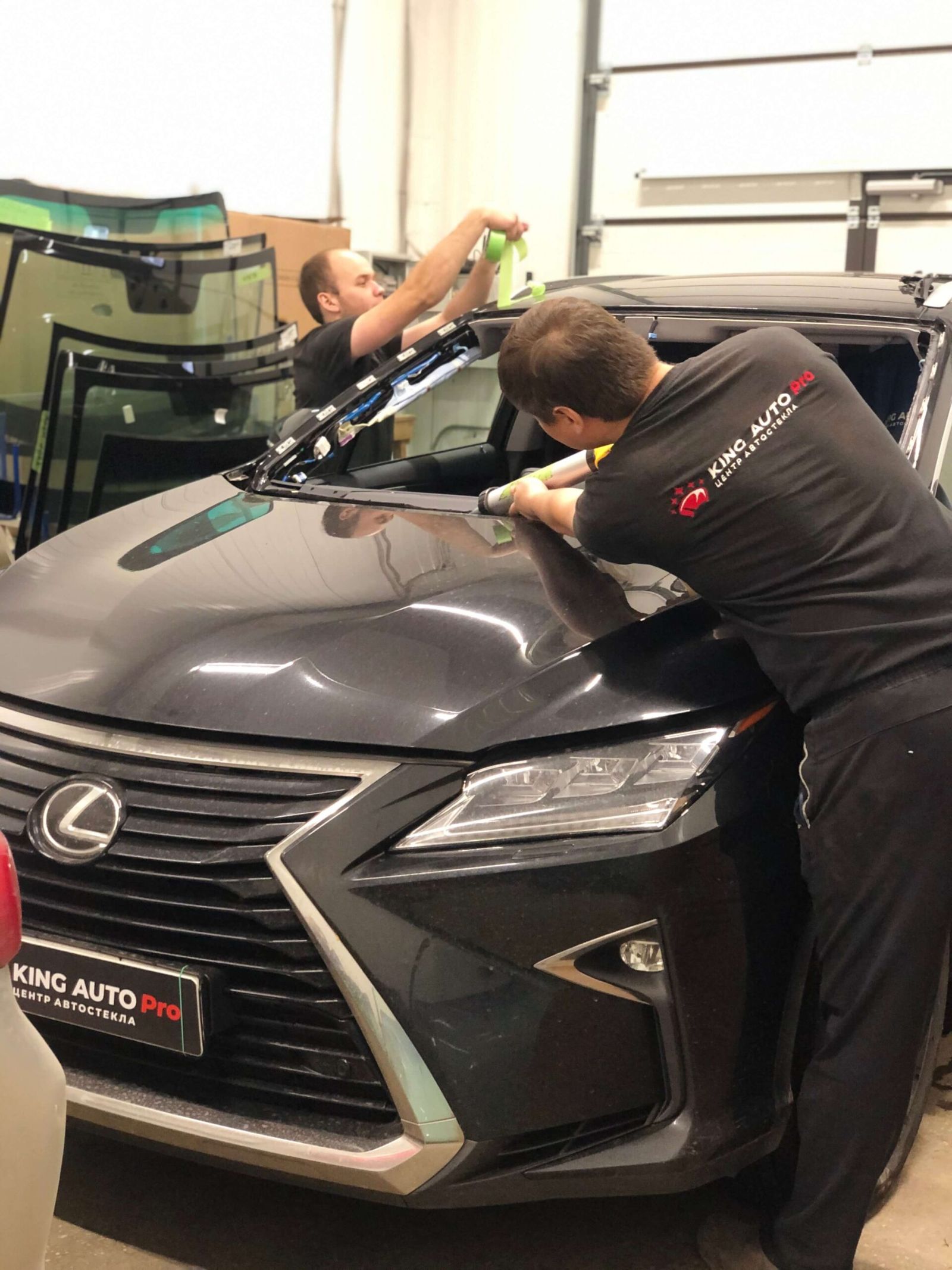 Двое мастеров в фирменной форме вклеивают лобовое стекло Lexus RX